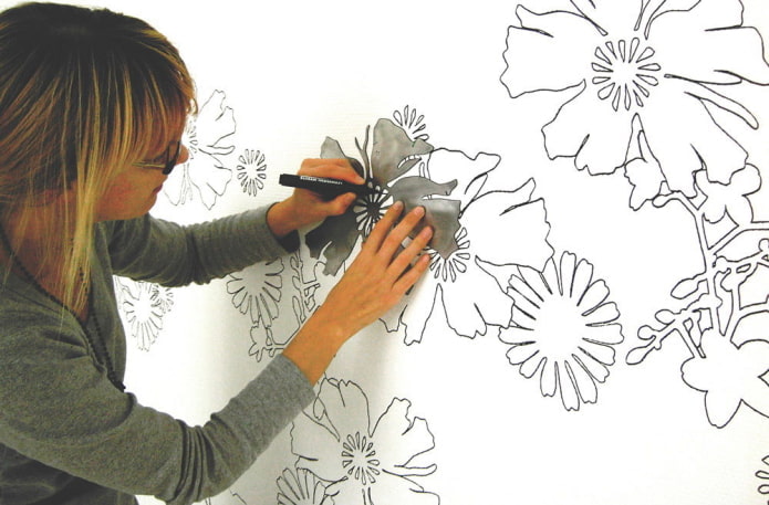mulher pintando flores na parede usando um estêncil
